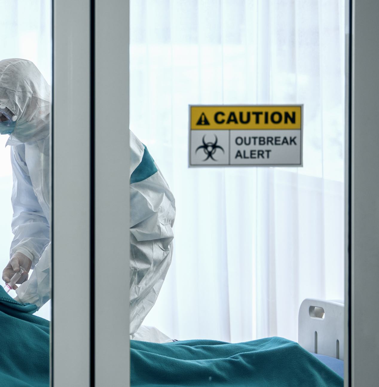 person in biohazard suit giving vaccination to patient in bed