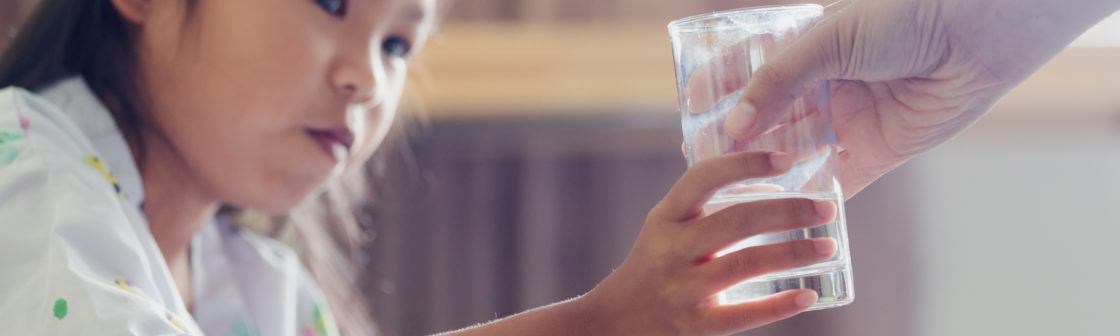 Close up on mother hand giving a glass of water to her sick daughter. Sick asian child drinking water after taking medicine