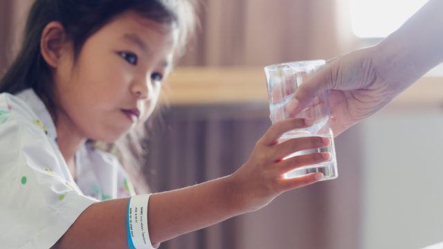 Close up on mother hand giving a glass of water to her sick daughter. Sick asian child drinking water after taking medicine