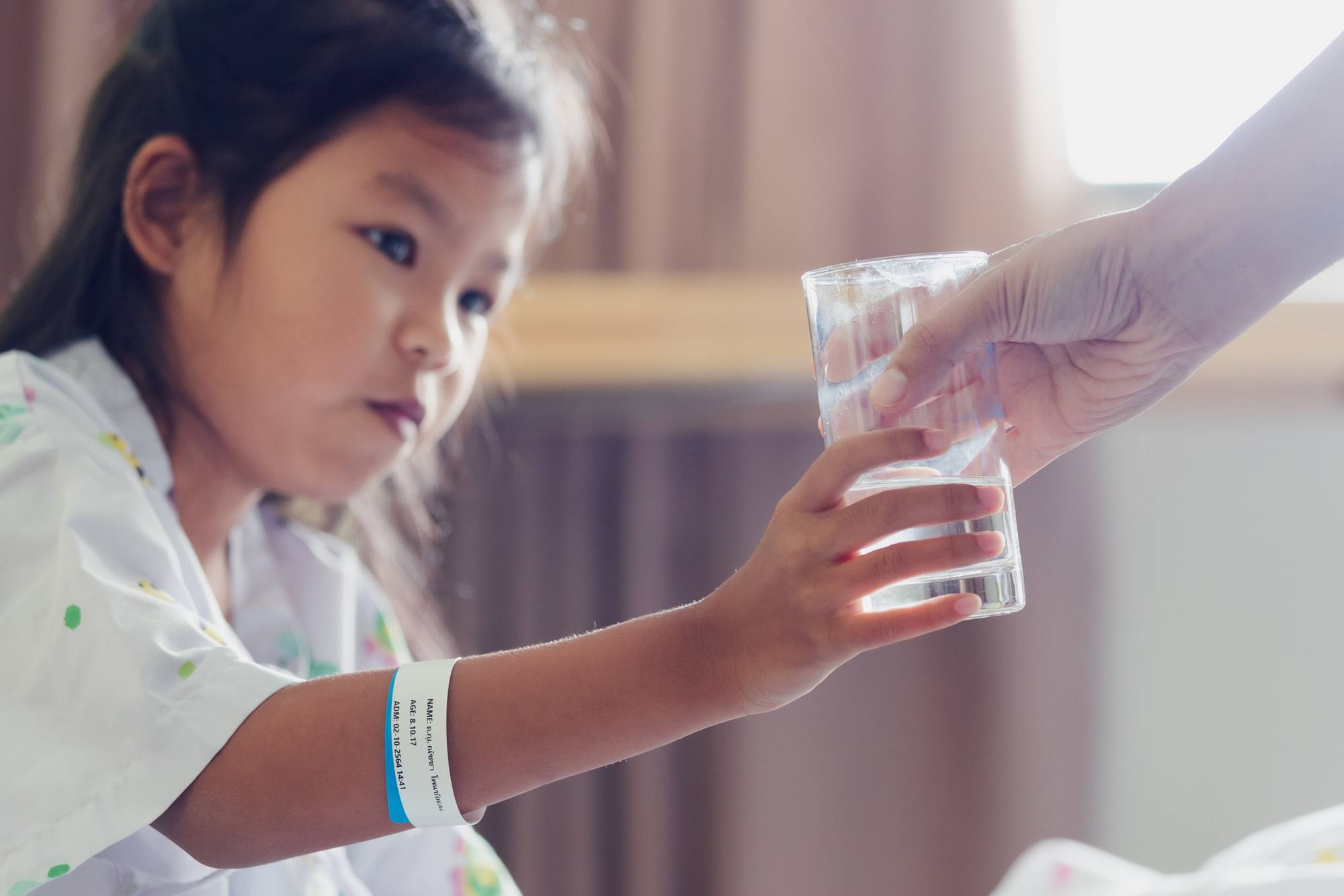 Close up on mother hand giving a glass of water to her sick daughter. Sick asian child drinking water after taking medicine