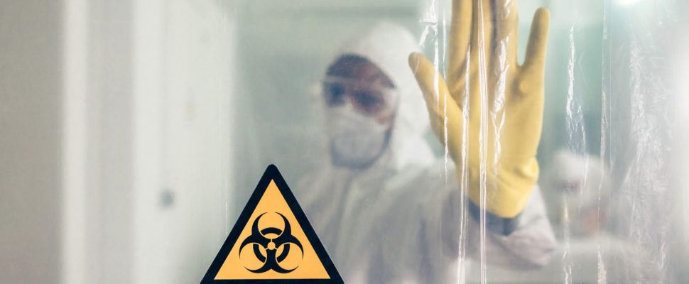 person in Biohazard suit behind plastic barrier